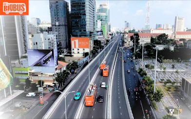 Open-top tour buses on a busy street in Ho Chi Minh City, showcasing urban architecture.