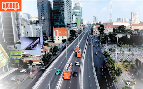 Open-top tour buses on a busy street in Ho Chi Minh City, showcasing urban architecture.