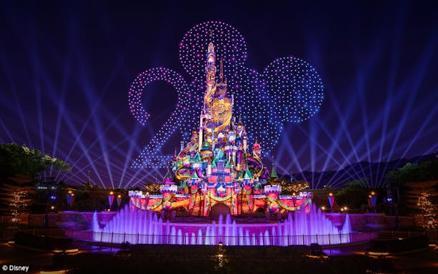 Hong Kong Disneyland castle with 20th anniversary decorations and fireworks in the night sky.