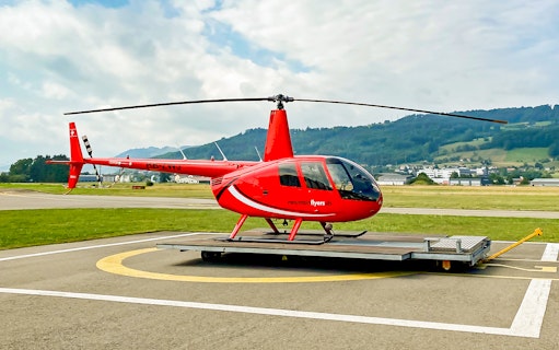 Red helicopter on helipad in Bern with scenic mountain backdrop.