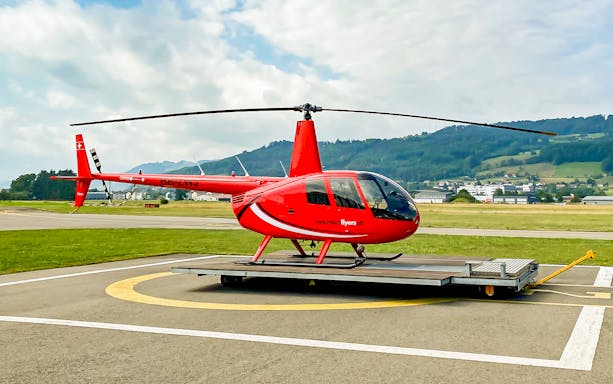 Red helicopter on helipad in Bern with scenic mountain backdrop.