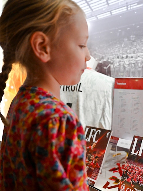 Young girl viewing signed Liverpool FC jersey at Anfield museum display.