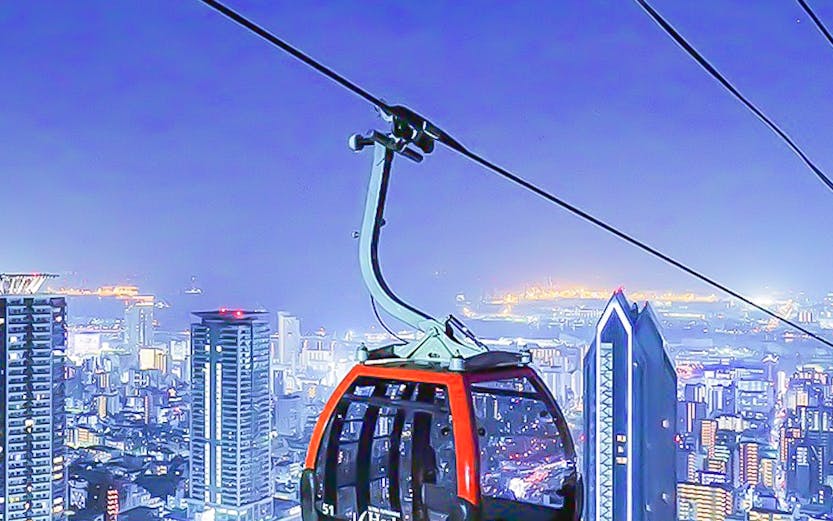Kobe Nunobiki Ropeway gondola over cityscape at night.