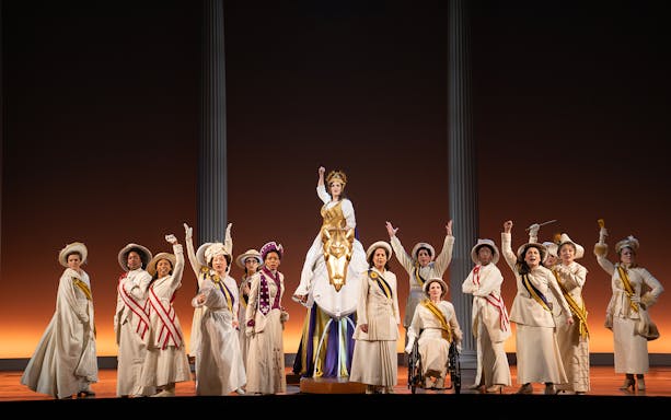 Performers in period costumes on stage during the show "Suffs" with a central figure on a horse.