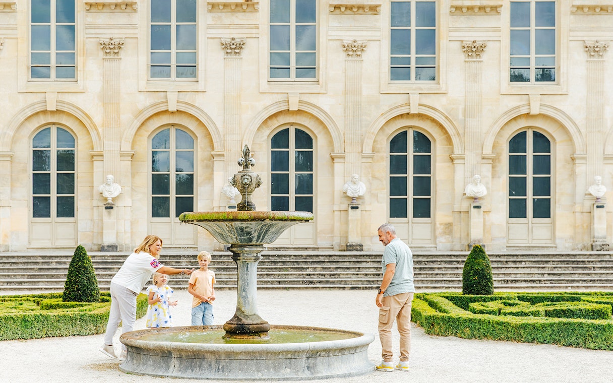 Family enjoying a fountain in the gardens of Chateau of Chantilly, France.