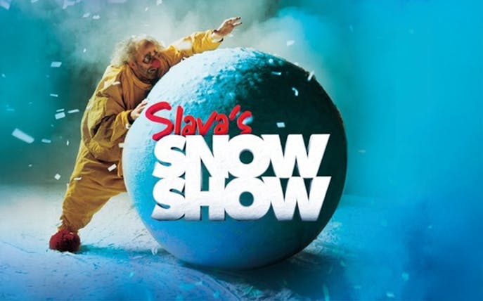 Performer in yellow suit with large snowball, Slava's Snowshow logo.