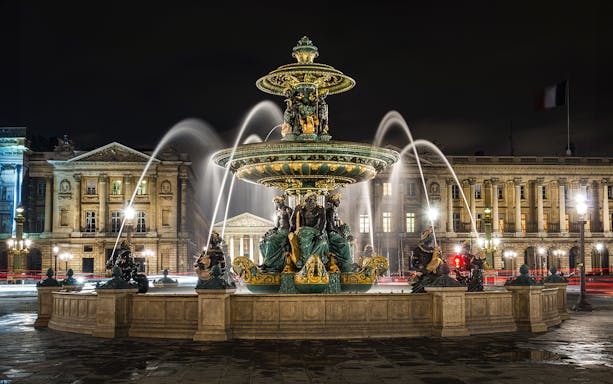 Fountain at Place de la Concorde in Paris at night with illuminated buildings.