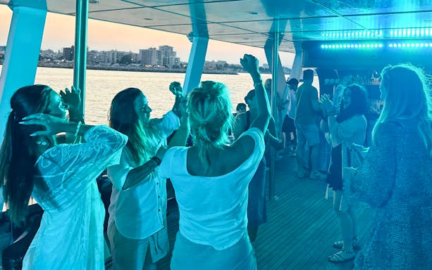 People dancing on a sunset cruise near Larnaca with city skyline in the background.