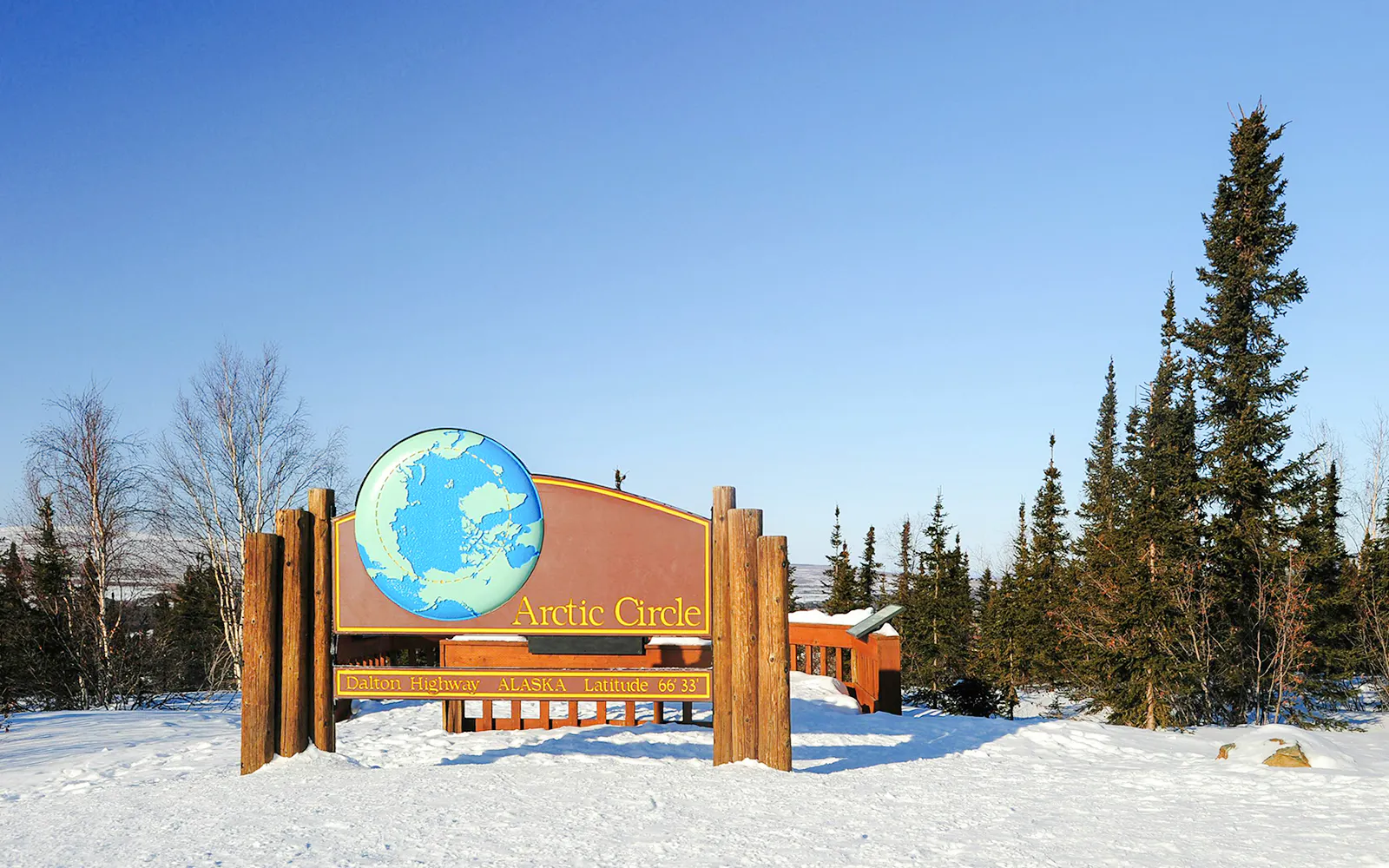 Arctic Circle sign on Dalton Highway, Alaska, surrounded by snow and trees.