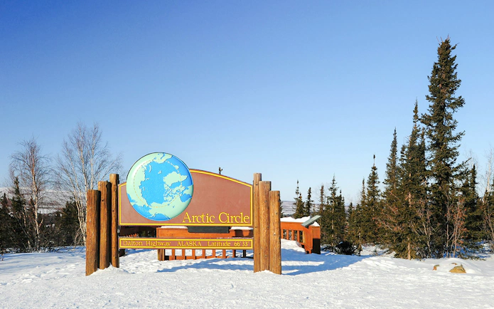 Arctic Circle sign on Dalton Highway, Alaska, surrounded by snow and trees.