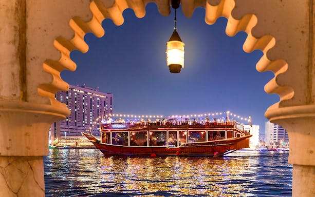 Pirate ship dhow cruise on Dubai Creek at night, framed by an archway.