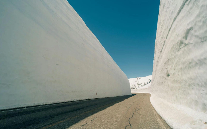 Yuki No Otani Snow Wall in Tateyama, Japan, towering over a clear road.