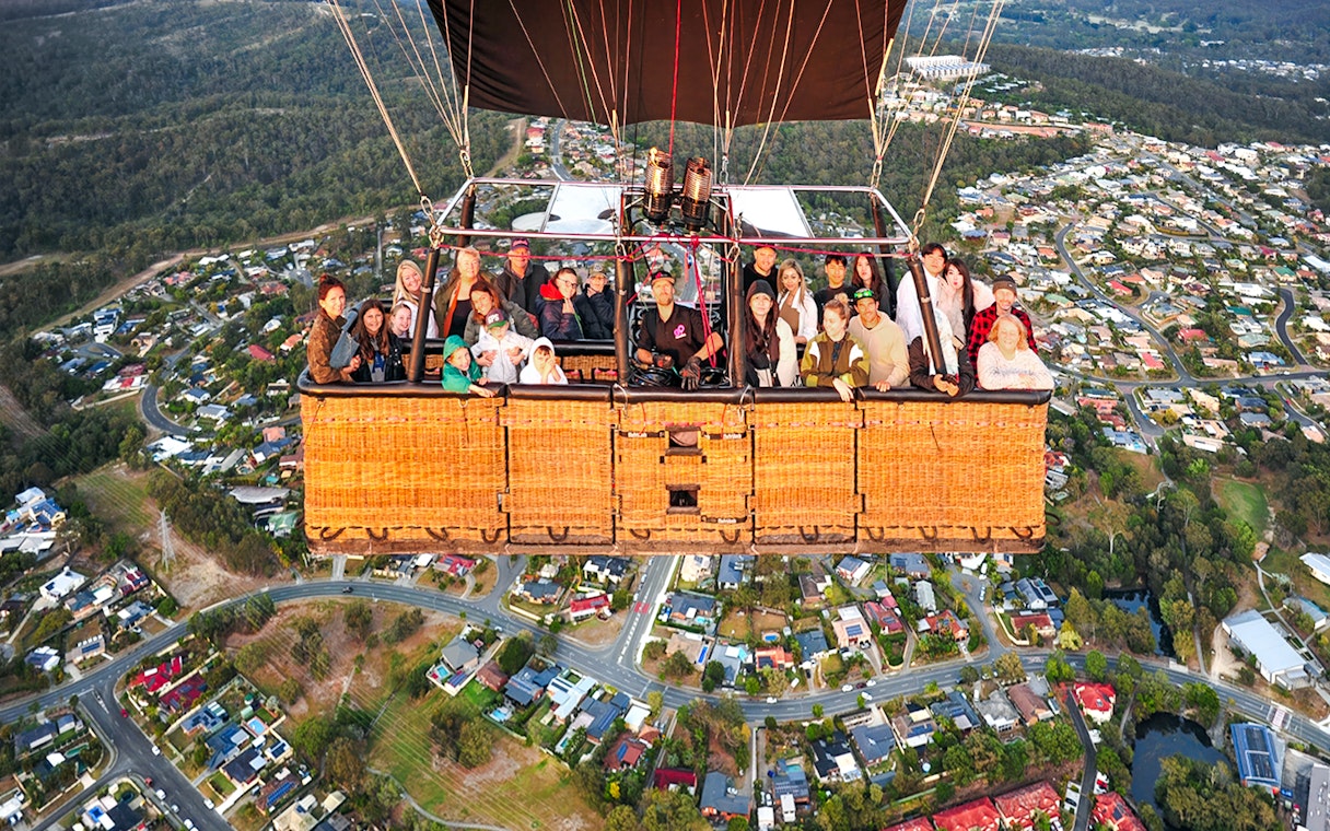 Group enjoying hot air balloon flight over suburban landscape.