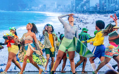 Performers in vibrant costumes dance at the Roxy Dinner Show in Rio de Janeiro, with a beach backdrop.