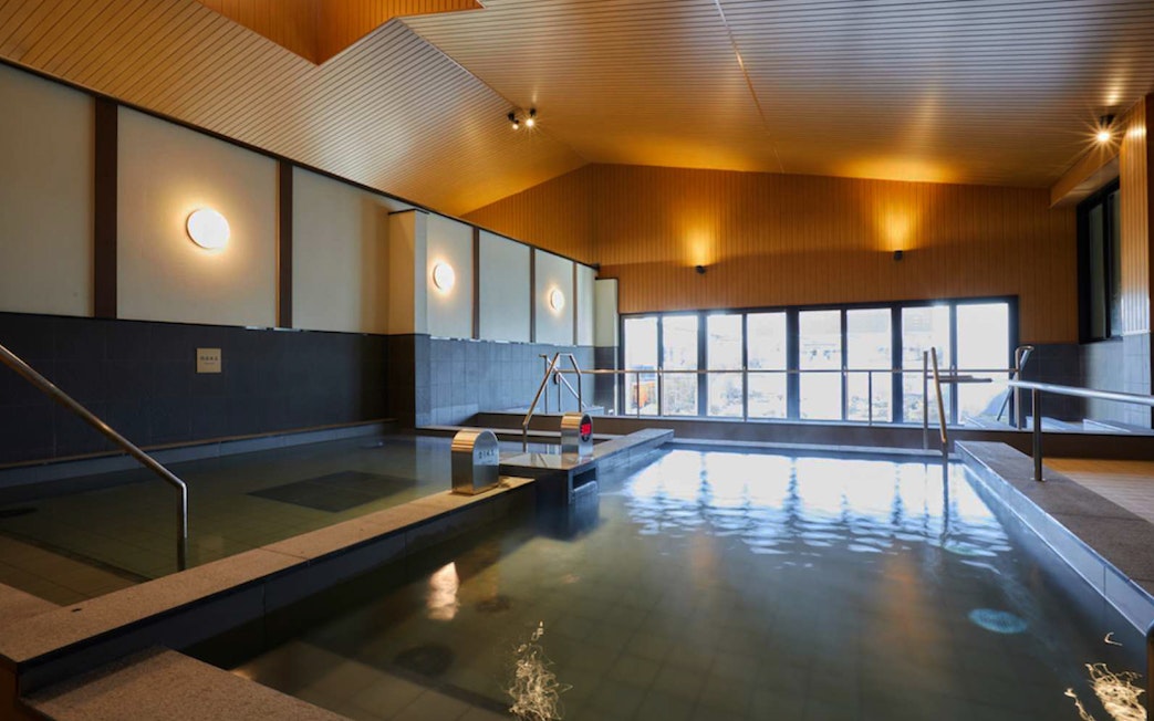 Indoor hot spring bath at Solaniwa Onsen with wooden ceiling and large windows.