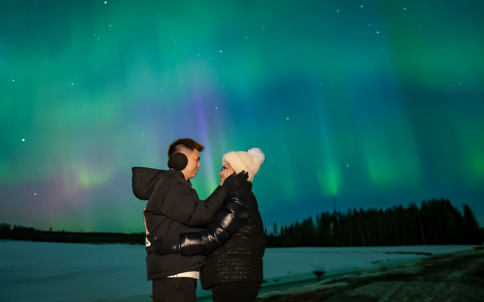 Couple embracing under Northern Lights in Rovaniemi.