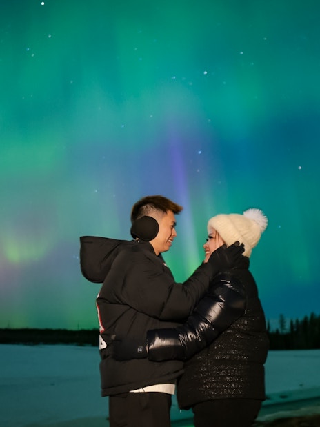 Couple embracing under Northern Lights in Rovaniemi.