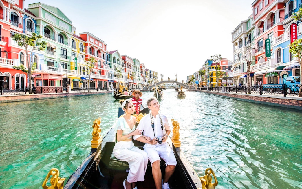 Couple enjoying a gondola ride on a canal in Venice with colorful buildings.