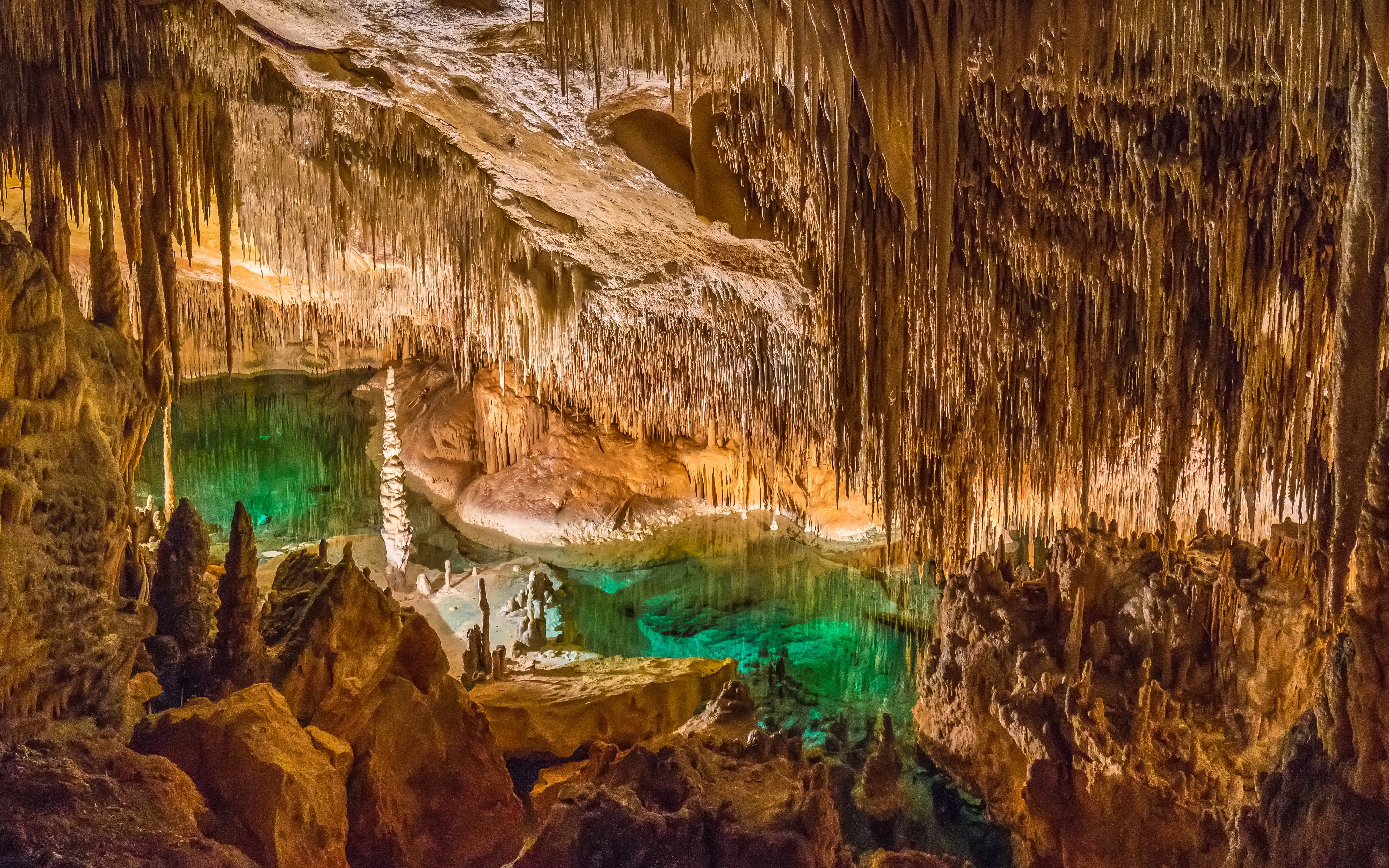 Stalactites and stalagmites in Drach Caves, Mallorca, with illuminated underground lake.