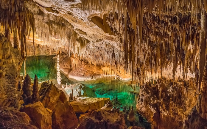 Stalactites and stalagmites in Drach Caves, Mallorca, with illuminated underground lake.