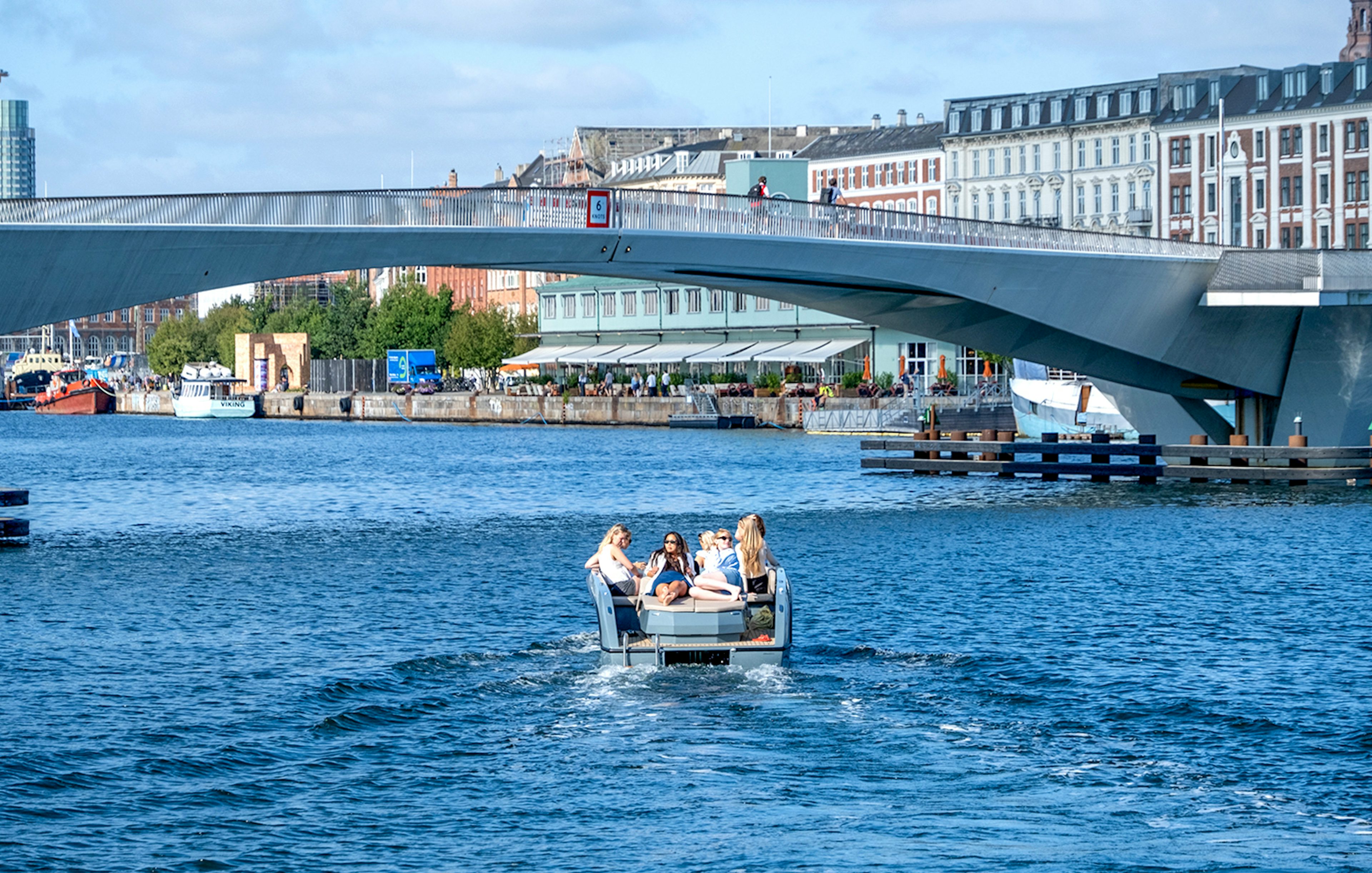 Guests on a boat tour in Copenhagen harbor, passing under a modern bridge.