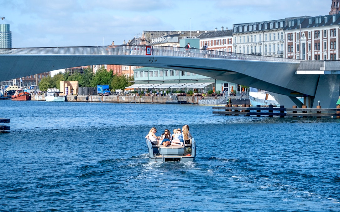 Guests on a boat tour in Copenhagen harbor, passing under a modern bridge.