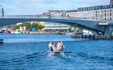 Guests on a boat tour in Copenhagen harbor, passing under a modern bridge.