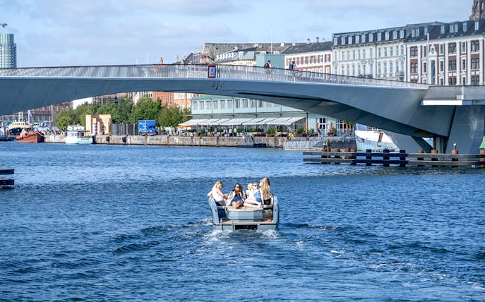 Guests on a boat tour in Copenhagen harbor, passing under a modern bridge.