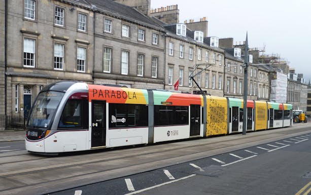 Edinburgh tram on city street for airport transfer.