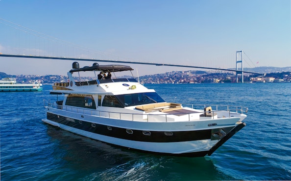 Luxury yacht cruising on the Bosphorus with Istanbul's skyline and bridge in the background.