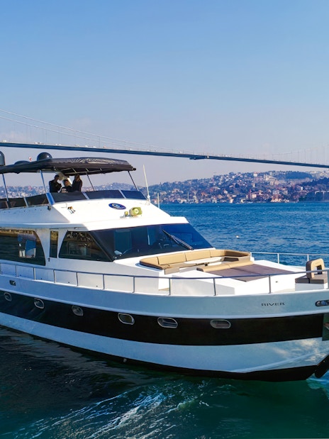 Luxury yacht cruising on the Bosphorus with Istanbul's skyline and bridge in the background.