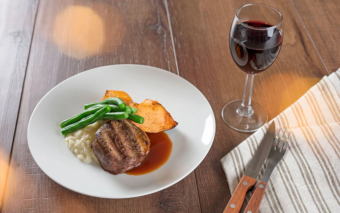 Steak dinner with green beans, sweet potato, and wine at Australian Outback Spectacular Heartland Show.