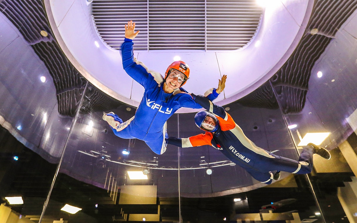 Indoor skydiving at iFLY with instructor guiding participant in wind tunnel.