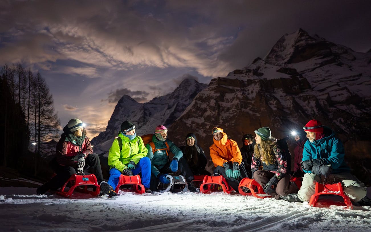 Group sledding at night in snowy Interlaken with mountains in the background.
