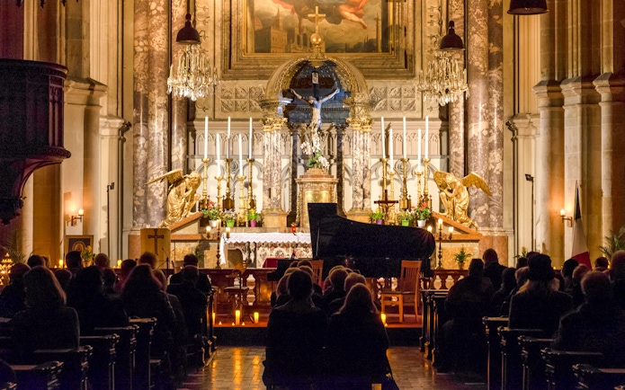 Classical concert audience at Minoritenkirche with grand piano and ornate altar.