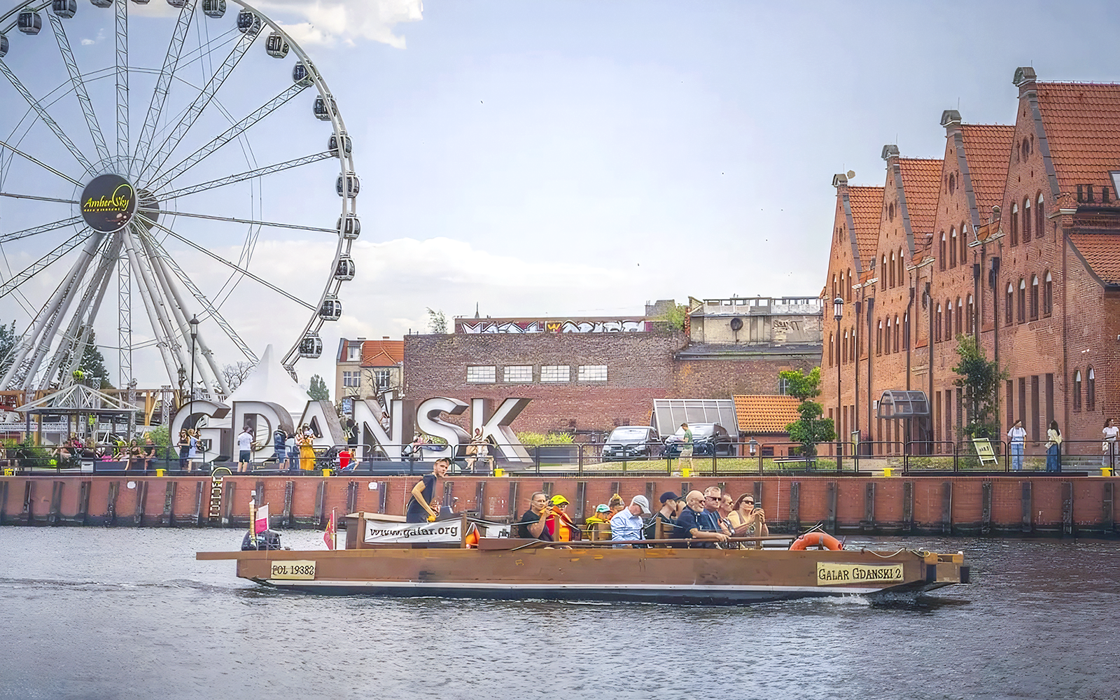 Galar boat cruising past Gdansk Ferris wheel and historic buildings.