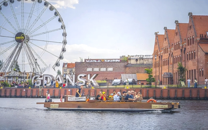 Galar boat cruising past Gdansk Ferris wheel and historic buildings.