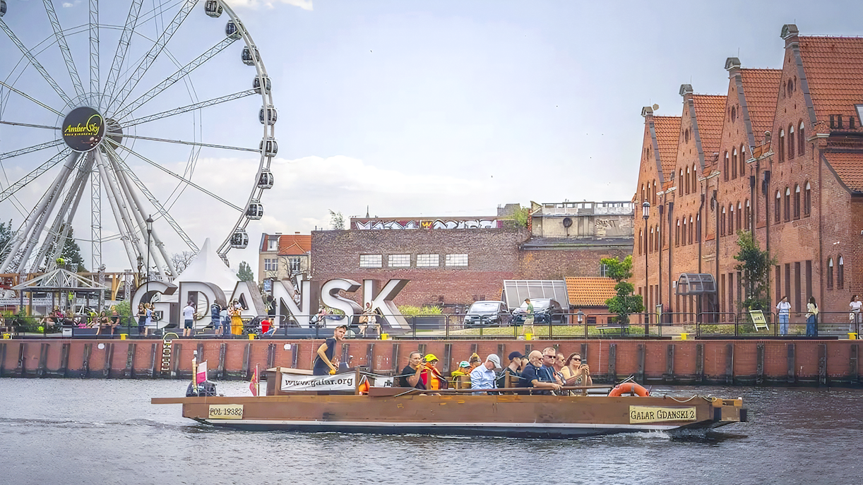 Galar boat cruising past Gdansk Ferris wheel and historic buildings.