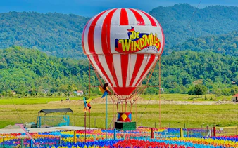 Hot air balloon at De Windmill Selfie Park, Langkawi, with colorful pinwheels and scenic mountain backdrop.