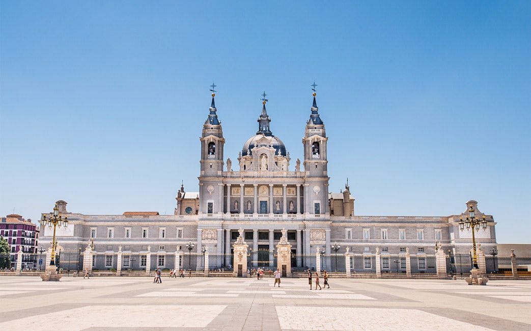 Almudena Cathedral facade in Madrid, Spain, with tourists in the foreground.