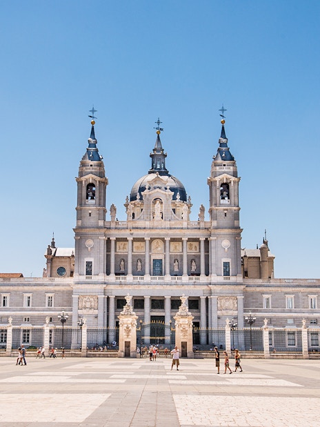 Almudena Cathedral facade in Madrid, Spain, with tourists in the foreground.