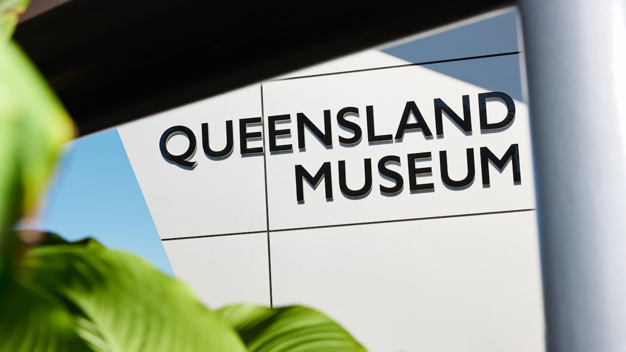Queensland Museum entrance sign with greenery in foreground.
