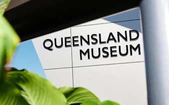 Queensland Museum entrance sign with greenery in foreground.