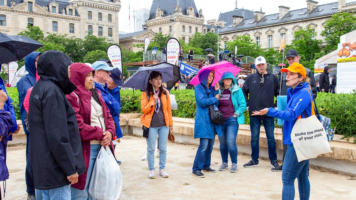 Tour group with guide near Notre Dame de Paris, umbrellas open, during outdoor walking tour.