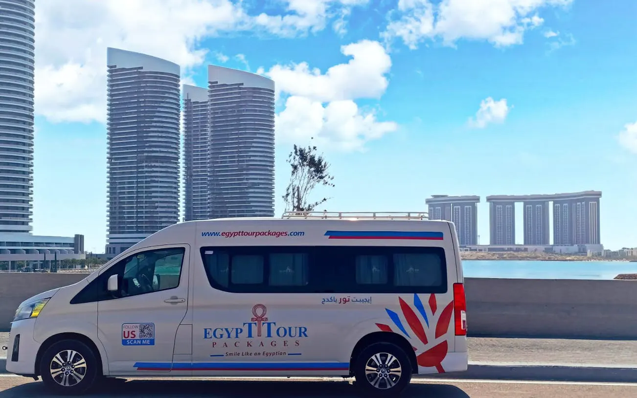 Private transfer van in front of modern buildings, Luxor to Hurghada route.