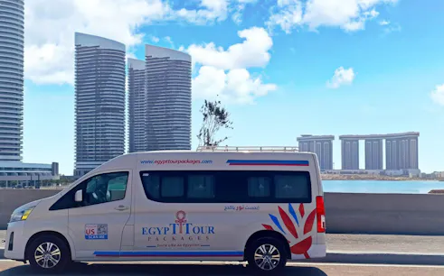 Private transfer van in front of modern buildings, Luxor to Hurghada route.