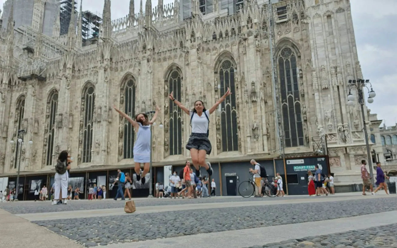 Two people jumping in front of Milan Cathedral during a self-guided city exploration game.