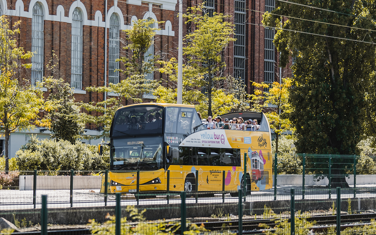 Yellow double-decker bus on Lisbon hop-on hop-off tour passing historic building.