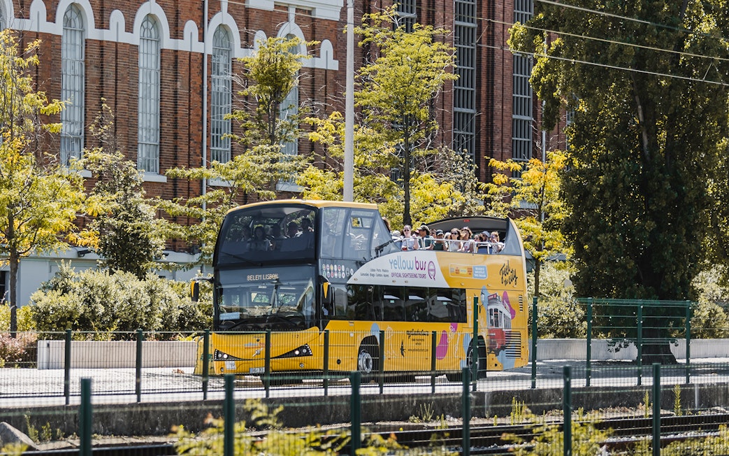 Yellow double-decker bus on Lisbon hop-on hop-off tour passing historic building.