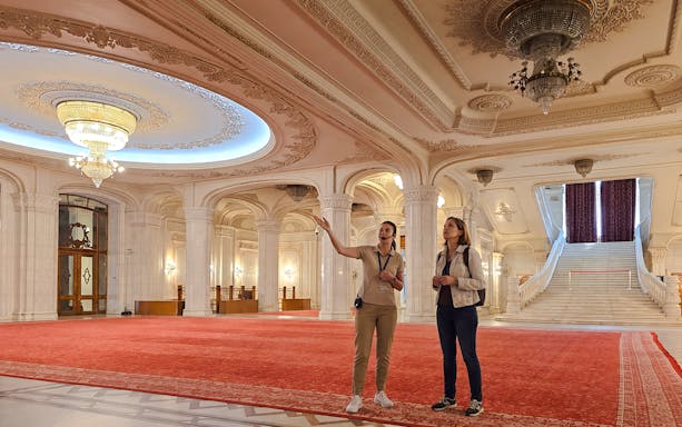 Tourists exploring ornate hall with chandeliers, Palace of Parliament, Bucharest.